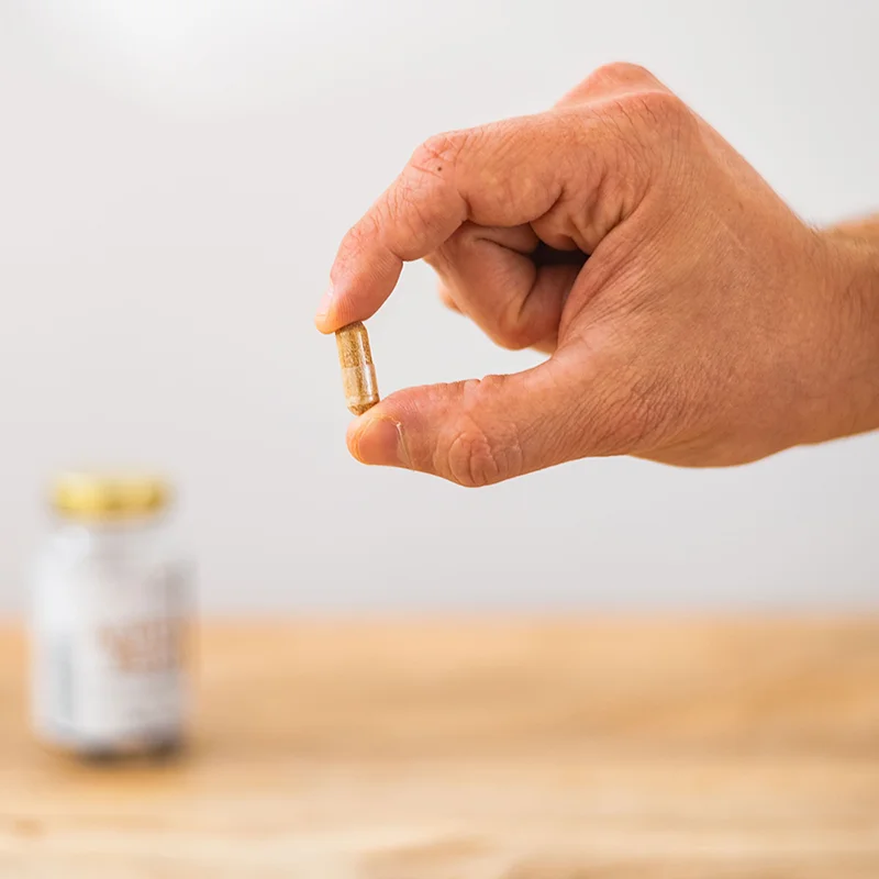 A single Active Move capsule held between fingers, with the bottle blurred in the background
